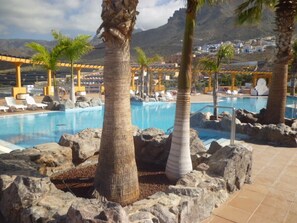 A pool area with palm trees, lounge chairs, and a mountainous backdrop. - Roque Del Conde (Costa Adeje)