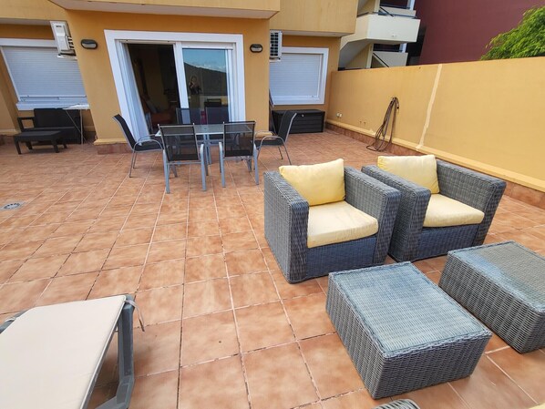 A patio with wicker furniture, a glass table, and chairs. - Roque Del Conde (Costa Adeje)