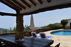 A poolside area with a stone table, two blue lounge chairs, and a view of the sea.