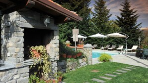 Un edificio in pietra con un camino, circondato da piante in vaso e una zona piscina con lettini e ombrelloni.