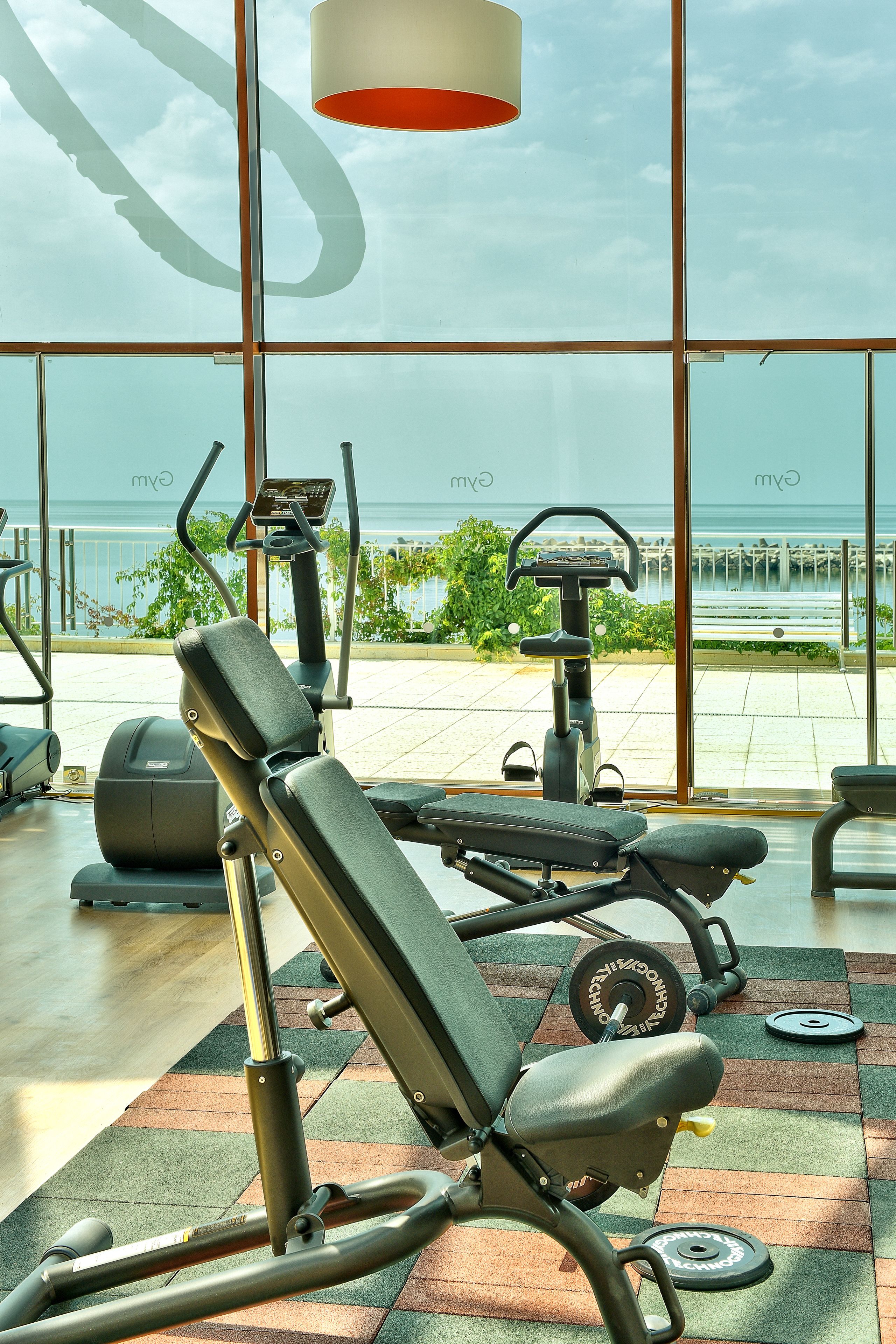 Un gimnasio con equipo de ejercicio y vistas al mar a través de amplias ventanas.