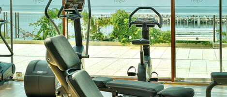Un gimnasio con equipo de ejercicio y vistas al mar a través de amplias ventanas.