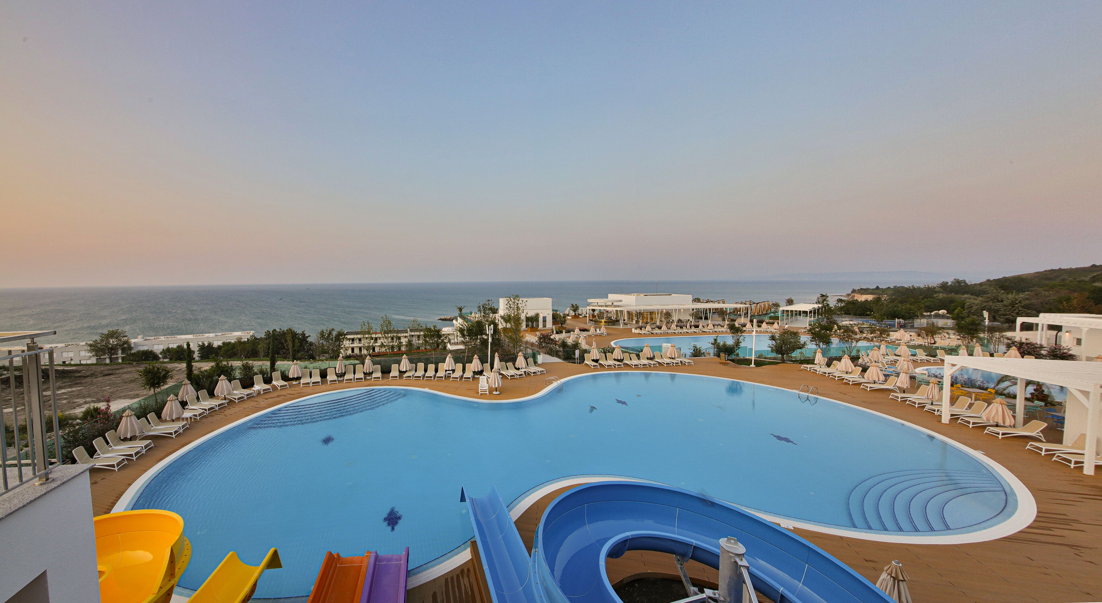 A large swimming pool with slides, sun loungers, and a view of the sea.
