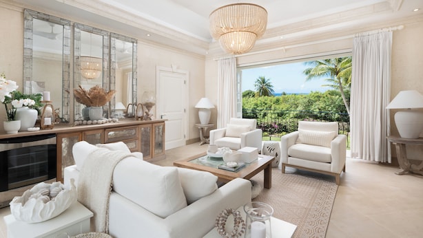 A spacious living room with a large window, white furniture, and a view of lush greenery. - Windfall, Westland Heights - Exclusive 5 bedroom villa, private chef (Westmoreland)