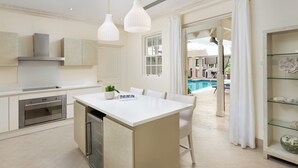 A modern kitchen with white cabinetry, a central island, pendant lighting, and a view of an outdoor swimming pool. - Windfall, Westland Heights - Exclusive 5 bedroom villa, private chef (Westmoreland)