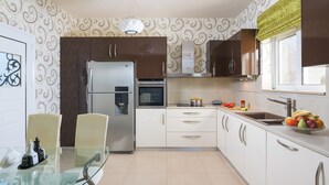 A modern kitchen with a refrigerator, oven, and sink. There is a dining table with chairs and a glass-top table. - Dreamcatcher Villa with private pool (Pastida)