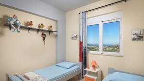 A bedroom with two single beds, a shelf with decorative items, a window with a view, and a curtain. - Dreamcatcher Villa with private pool (Pastida)