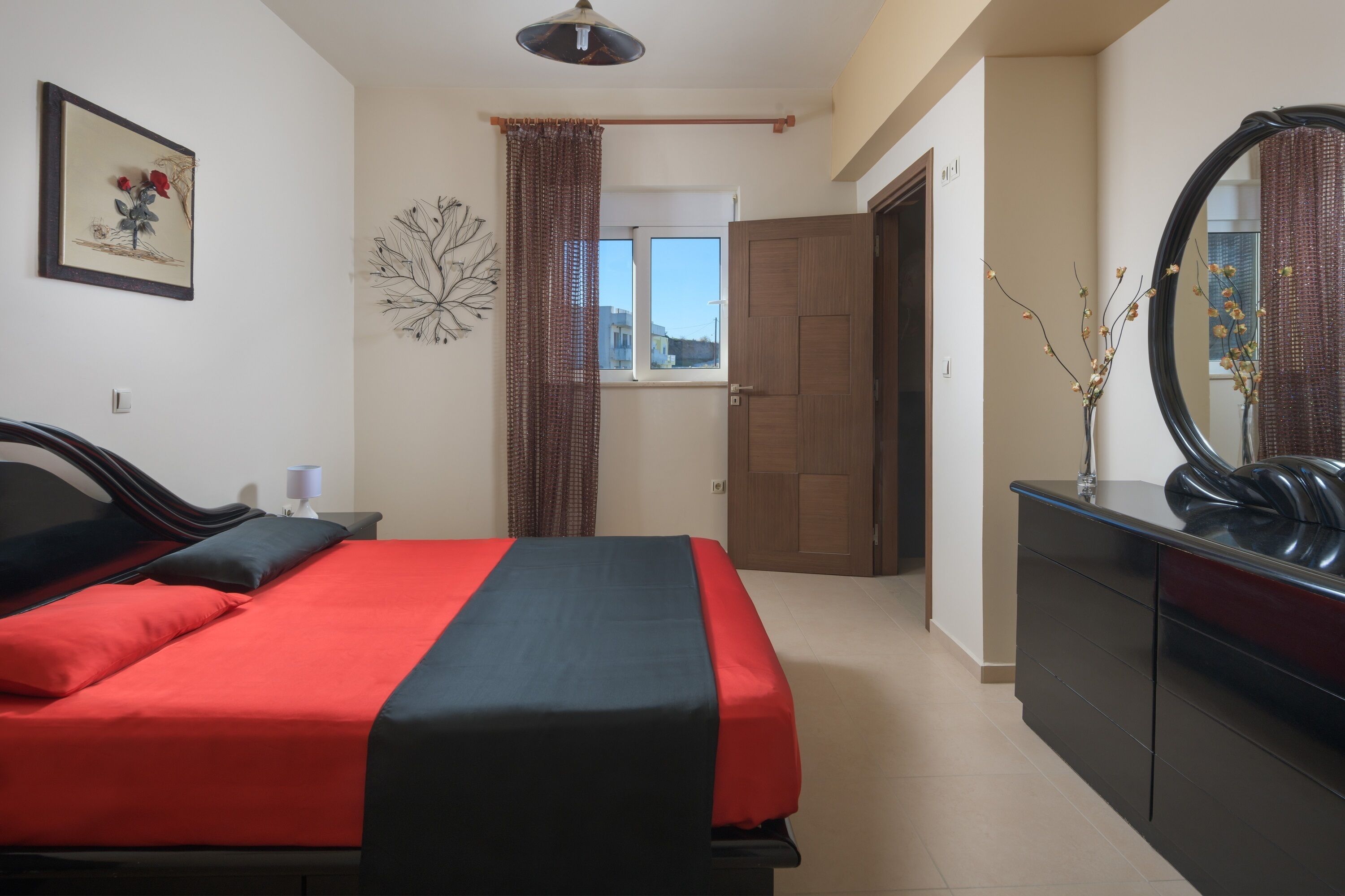 Un dormitorio con cama, cómoda, espejo, ventana con cortinas y puerta.