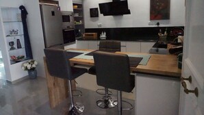 Una cocina moderna con una mesa de comedor de madera, dos taburetes tipo barra, horno empotrado y salpicadero negro.