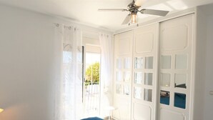 Un dormitorio con cama, ventilador de techo, ventana con cortinas y armario con puertas espejadas.