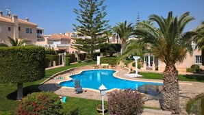 Una piscina rodeada de jardines bien cuidados, palmeras y un cielo azul despejado.