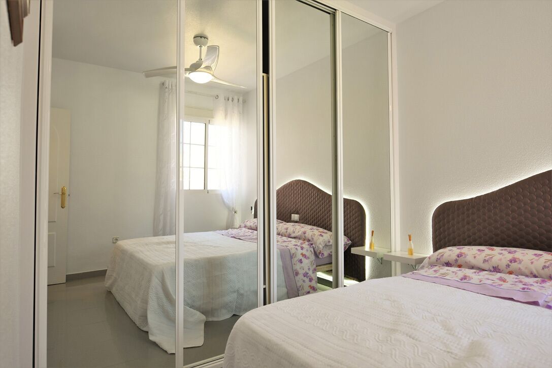 Un dormitorio con dos camas, un espejo, un ventilador de techo y una ventana con cortinas.