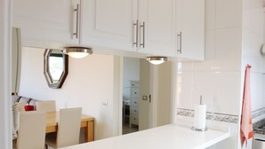Une cuisine moderne avec des meubles blancs, un coin repas comprenant une table et des chaises, et un couloir bien visible qui mène aux autres pièces.