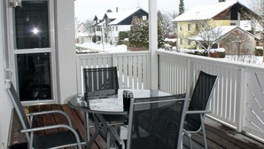 Ein überdachter Außenbereich mit Tisch und Stühlen, einer Holzterrasse und Blick auf verschneite Häuser im Hintergrund.
