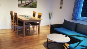 Ein Zimmer mit einem Holzesstisch, vier Stühlen, einem blauen Sofa und einem kleinen runden Tisch.