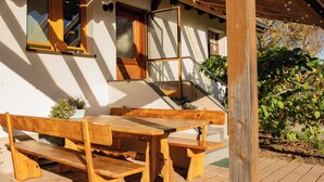 Un espace extérieur aménagé avec des meubles en bois, comprenant une table et des bancs, un escalier en bois et un pot de fleurs.