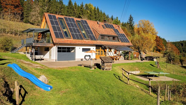 Une maison avec un toit en pente, des panneaux solaires, un garage et un toboggan dans un espace herbeux.