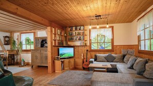 L’intérieur d’un chalet en bois chaleureux et accueillant, avec une télévision, des étagères à livres, une guitare et un canapé.