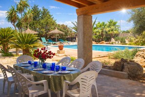 An outdoor dining area with a pool, palm trees, and a thatched-roof structure.
