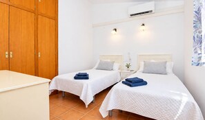 A hotel room with two beds, a wardrobe, an air conditioning unit, and a nightstand with a lamp.