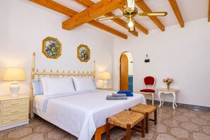 A hotel room with a bed, bedside lamps, a wooden headboard, a ceiling fan, a mirror, a red chair, a small table with a vase, and a hexagonal patterned floor. - Can Bril 409 rustic finca with private pool, terrace, garden and WiFi (Campos)