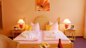 A double bed with white linens, two bedside tables with lamps, a wooden headboard, and a painting of a flower on the wall.