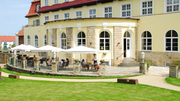 A yellow building with stone pillars and arched windows, featuring outdoor seating with umbrellas. - Kurhotel Fürstenhof (Blankenburg)