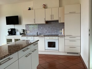 A kitchen with white cabinets, a tiled backsplash, a stove, and a flat-screen TV mounted on the wall.