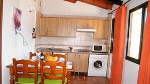Une cuisine compacte dotée de meubles en bois, d’un lave-linge, d’un four à micro-ondes et d’une table à manger avec des chaises.