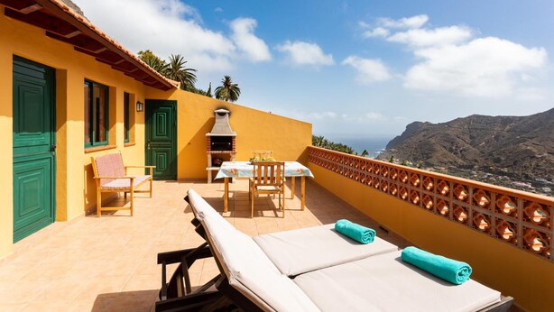Un balcon avec une table et des chaises, un barbecue et une vue sur les montagnes.