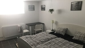 Quarto com cama, escrivaninha, cadeira, radiador e duas molduras na parede.