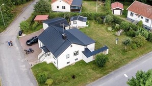 Um bairro residencial com uma grande casa branca, com telhado escuro, cercada por vegetação e outras casas.
