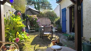 Une terrasse avec une table et des chaises, entourée de plantes en pot et d’une clôture en bois.