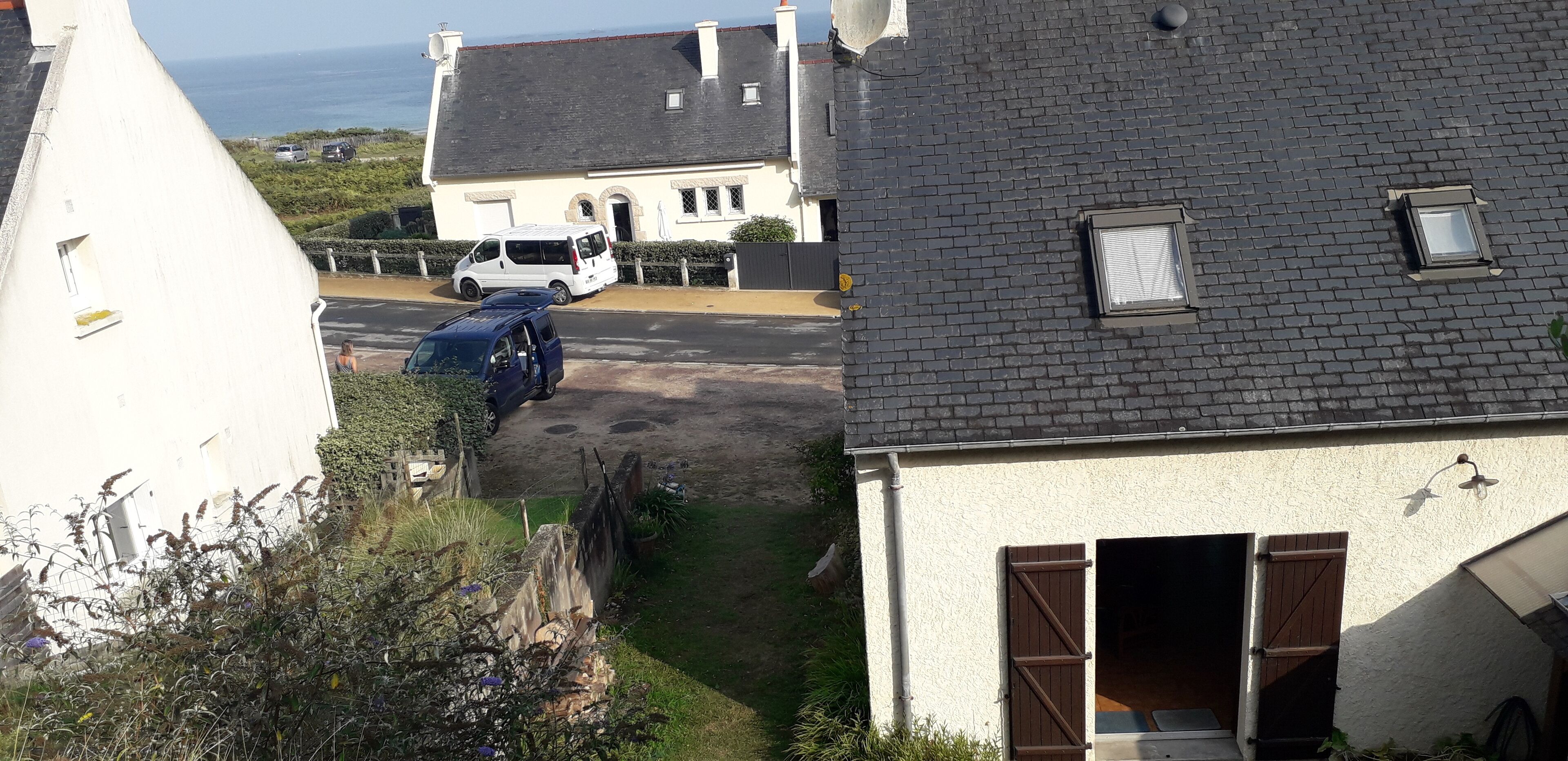 Ein Wohngebiet mit einem weißen Haus, einem blauen Lieferwagen und einem weißen Transporter, die an der Straße geparkt sind.
