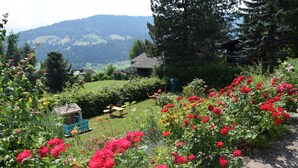 A garden with red flowers, a wooden bench, and a small birdhouse. - Landhaus Mitsche, Gartnerkofel apartment with mountain views (Radnig)