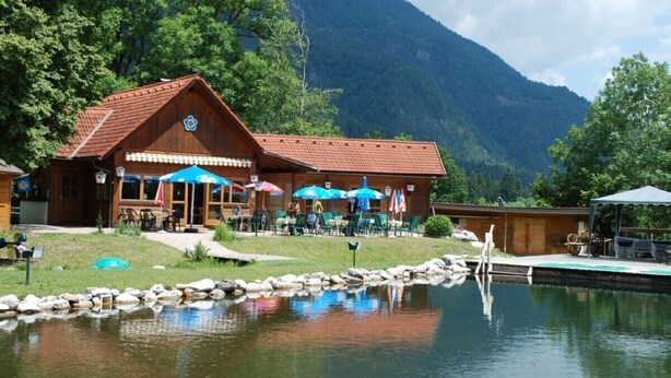 A wooden lodge with outdoor seating and a pond in front. - Landhaus Mitsche, Gartnerkofel apartment with mountain views (Radnig)
