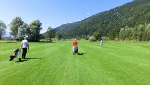 A golf course with a clear sky, a hilly backdrop, and a person walking with a golf bag. - Landhaus Mitsche, Gartnerkofel apartment with mountain views (Radnig)