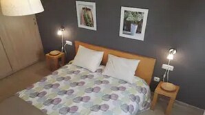 Un dormitorio con una cama, dos mesitas de noche, una lámpara y dos cuadros en la pared.