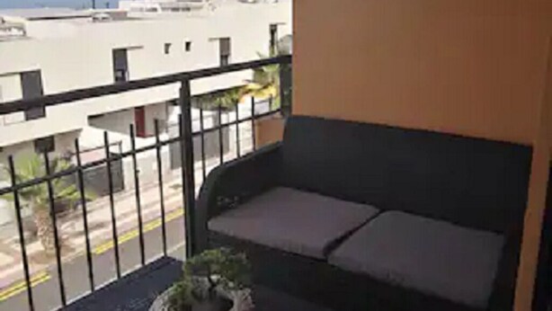 Un balcón con una mesa negra, una planta en maceta y un sofá con cojines.