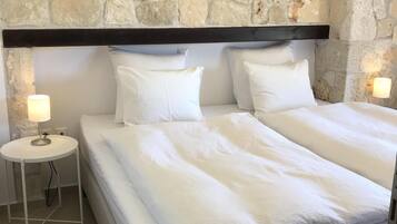 A double bed with white bedding in a room with a stone wall and a wooden headboard.