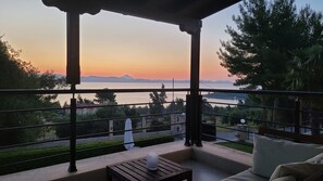 Ein Balkon mit Blick auf einen Sonnenuntergang über einem Gewässer, umgeben von Bäumen und einem entfernten Gebirgszug.