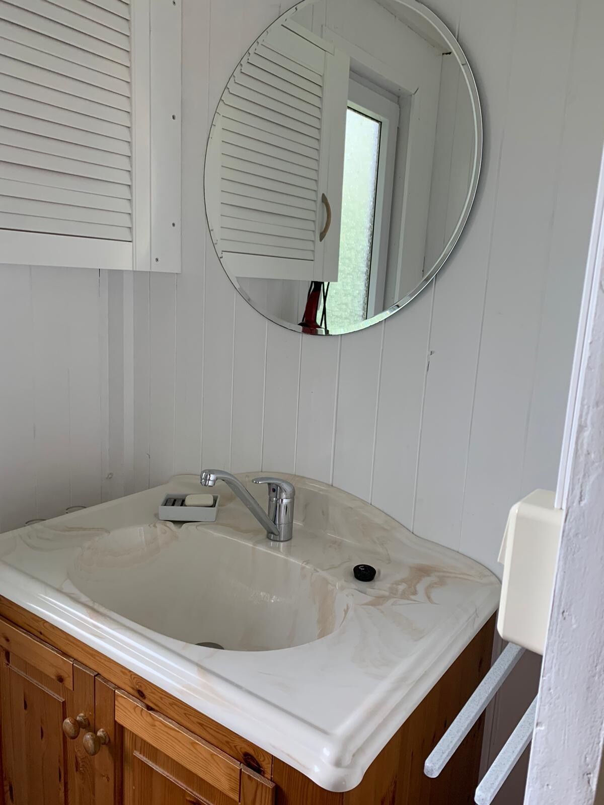 Un baño con un lavamanos blanco, un espejo redondo y armarios de madera.