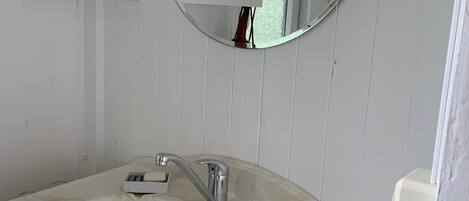 Un baño con un lavamanos blanco, un espejo redondo y armarios de madera.