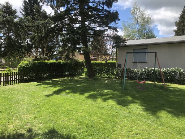Un patio césped cuidado con un columpio y una pequeña construcción con una ventana.