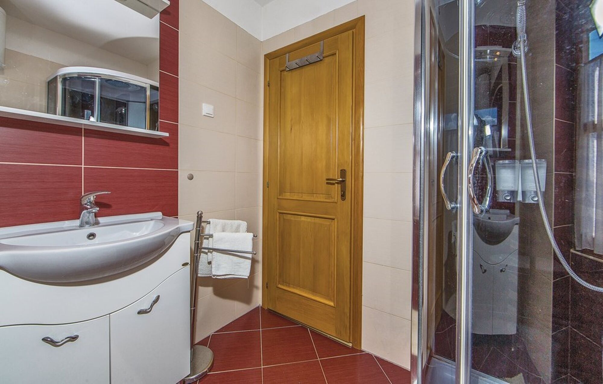 Une salle de bain avec un lavabo, un miroir, une porte en bois et un espace douche.