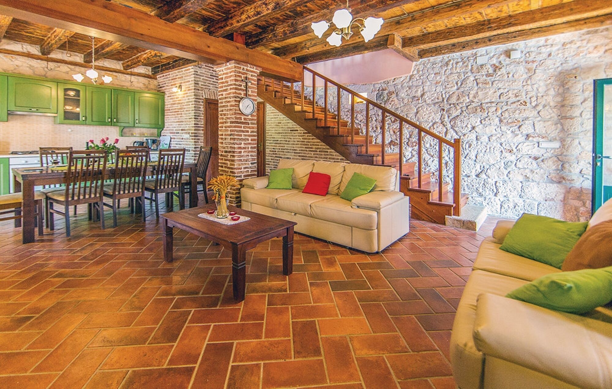 Amplia sala de estar con escalera de madera, un sofá con cojines verdes y un juego de comedor.