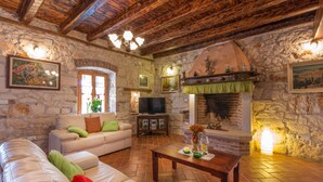 A cozy living room with stone walls, a fireplace, a sofa, and a television. - Beautiful villa with pool, KA, barbecue, WLAN, suitable for families (Fuskulin)