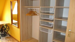 A room with a wooden floor, a wooden wardrobe with open shelves, and a mirror on the wall.