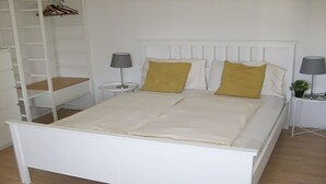 En vit säng med två kuddar, ett sängbord med en lampa och en vit garderob med en hylla.