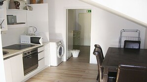 Ett kompakt kök med mikrovågsugn, spis och tvättmaskin. Här finns ett matbord med stolar och en synlig utgångsdörr.